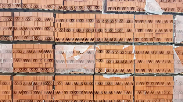 Red perforated bricks with rectangular holes on wooden pallets in an open-air warehouse ready for sale. New bricks on pallets at a hardware store