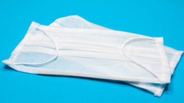 Ağzı ve burnu mavi arka planda tutmak için plastik pedli üç katmanlı tek kullanımlık cerrahi maske. Bakterilerden, sağlık hizmetlerinden ve tıptan korunma kavramı. COVID-19