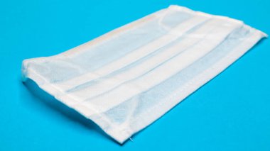 Bir adet 3 katlı tek kullanımlık cerrahi yüz maskesi. Ağzını ve burnunu kaplayan lastik kabzalı mavi arka plan. Bakterilerden, sağlık hizmetlerinden ve tıp konseptinden korunma. COVID-19. Tehlikeli bir virüs.