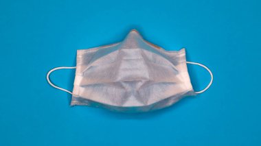 Bir adet 3 katlı tek kullanımlık cerrahi yüz maskesi. Ağzını ve burnunu kaplayan lastik kabzalı mavi arka plan. Bakterilerden, sağlık hizmetlerinden ve tıp konseptinden korunma. COVID-19. Tehlikeli bir virüs.