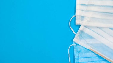 Mavi arka plandaki ağız ve burnu kapatmak için plastik pedlerle tek kullanımlık üç yüz maskesi. Bakterilerden, sağlık hizmetlerinden ve tıptan korunma kavramı. COVID-19. Boşluğu kopyala.