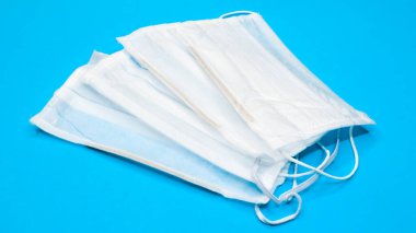 Mavi arka plandaki ağız ve burnu kapatmak için plastik pedlerle tek kullanımlık üç yüz maskesi. Bakterilerden, sağlık hizmetlerinden ve tıptan korunma kavramı. COVID-19. Tehlikeli bir virüs..