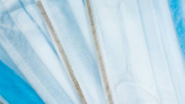 Coronavirus koruması. Birçok antiviral koruyucu tıbbi yüz maskesi ve mavi arka planda kulak halkaları var. Cerrahi maske geçmişi. Solunum sendromu, koronavirüs hastalığı COVID-19.