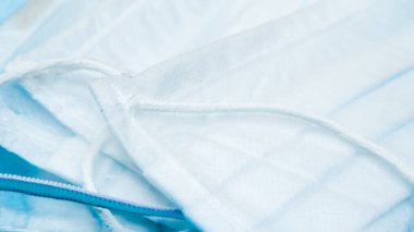 Coronavirus koruması. Birçok antiviral koruyucu tıbbi yüz maskesi ve mavi arka planda kulak halkaları var. Cerrahi maske geçmişi. Solunum sendromu, koronavirüs hastalığı COVID-19.