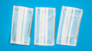 Mavi arka plandaki ağız ve burnu kapatmak için plastik pedlerle tek kullanımlık üç yüz maskesi. Bakterilerden, sağlık hizmetlerinden ve tıptan korunma kavramı. COVID-19. Tehlikeli bir virüs..
