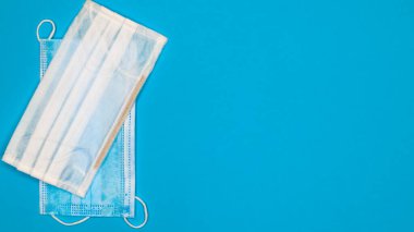 Mavi arka plandaki ağız ve burnu kapatmak için plastik pedlerle tek kullanımlık iki yüz maskesi. Bakterilerden, sağlık hizmetlerinden ve tıptan korunma kavramı. COVID-19. Boşluğu kopyala.