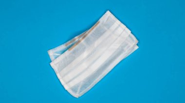 Ağzı ve burnu mavi arka planda tutmak için plastik pedli üç katmanlı tek kullanımlık cerrahi maske. Bakterilerden, sağlık hizmetlerinden ve tıptan korunma kavramı. COVID-19.