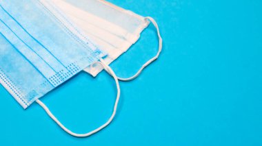 Mavi arka plandaki ağız ve burnu kapatmak için plastik pedlerle tek kullanımlık iki yüz maskesi. Bakterilerden, sağlık hizmetlerinden ve tıptan korunma kavramı. COVID-19. Boşluğu kopyala.