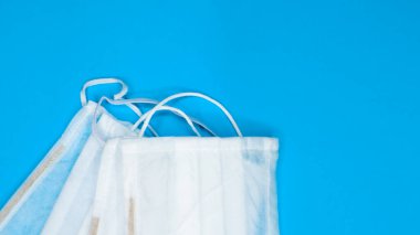 Mavi arka plandaki ağız ve burnu kapatmak için plastik pedlerle tek kullanımlık üç yüz maskesi. Bakterilerden, sağlık hizmetlerinden ve tıptan korunma kavramı. COVID-19. Boşluğu kopyala.
