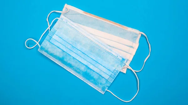 Two three-layer disposable surgical face masks with rubber pads to cover the mouth and nose against a blue background. The concept of protection from bacteria, healthcare and medicine. COVID-19.