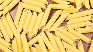 Penne Rigate Raw Pasta, eğimli kesimli ve kaburgalı yüzeyi olan kısa bir makarnadır. Geleneksel İtalyan makarnası. Makarna arka planı. Kahverengi masadaki İtalyan yemek malzemelerinin üst görüntüsü