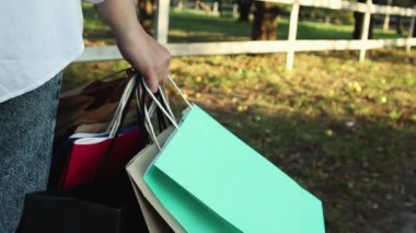 Açık hava alışveriş merkezinden alışveriş yaptıktan sonra renkli kağıt torbalarla bir kadın müşterinin elini yakın plan çekeceğiz. Kara Cuma, alışveriş ve Noel hediyeleri kavramı. Alışveriş kolikleri ve alışveriş torbaları..