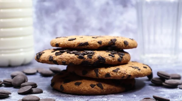 American chocolate chip cookies stacked on top of each other with milk in a glass on a gray background. Traditional rounded crunchy dough with chocolate chips. Bakery. Delicious dessert, pastries