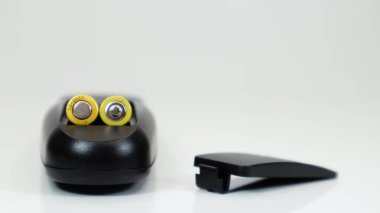 Beyaz arka planda sarı AAA pilleri olan siyah uzaktan kumanda. Batarya değiştirme, yedek parça. Uzaktan kumandalı batarya bölmesi.