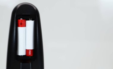 Beyaz arka planda kırmızı ve beyaz AAA alkalin pilli siyah TV uzaktan kumandası. Batarya değiştirme, yedek parça. Uzaktan kumandalı batarya bölmesi. Boşluğu kopyala.