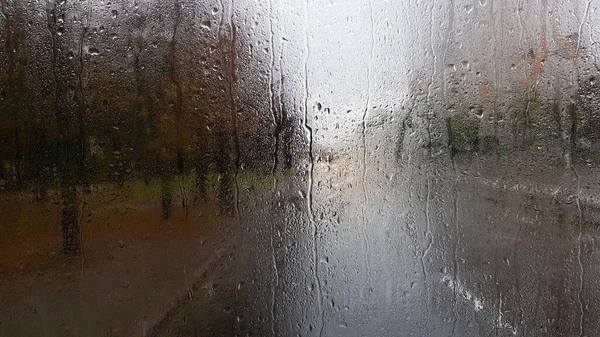 Rain on the rear window of a car in autumn. Inside view of the road with moving cars in the city through the window from the car with rain drops. driving a car in the field of view of the rear window