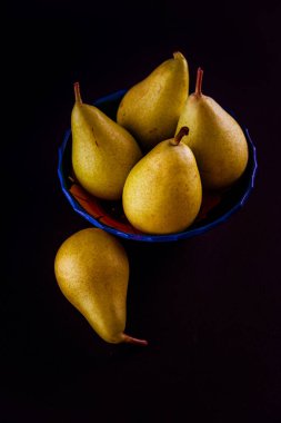 Seramik kasedeki taze doğal armutlar beyaz masa örtüsü üzerine elle dekore edilmiş.
