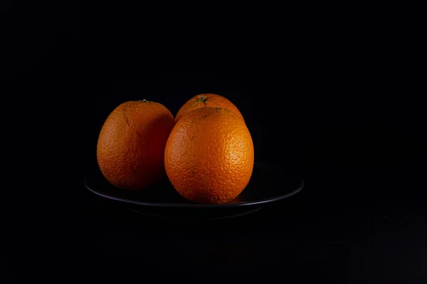 Fresh seasonal oranges on black plate on black background