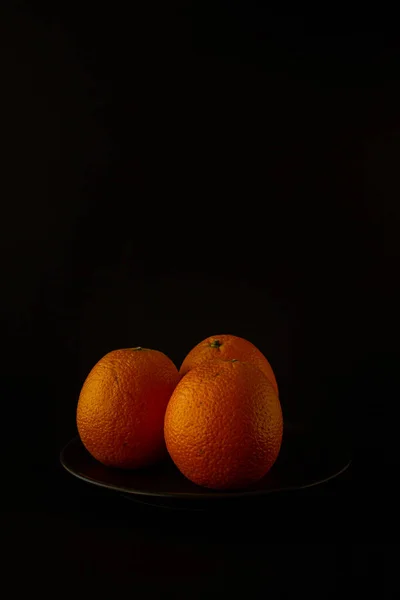 Fresh seasonal oranges on black plate on black background