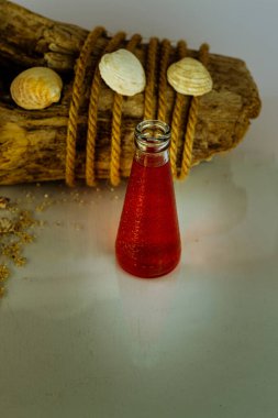 Taze kırmızı meyve suyu, kabuklar ve arka planda eski kütükler, deniz ve tatil konsepti olan bir şişe.