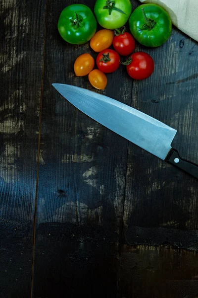 still life with fresh red, green and yellow tomatoes freshly picked from the garden on the wooden table and kitchen knife