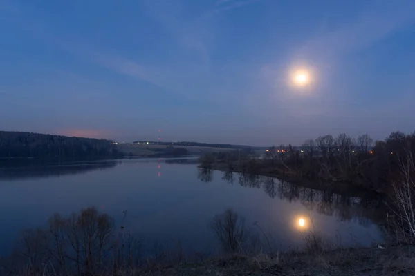 Big full moon in the blue sky over the lake at night