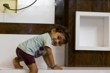 Küçük bir çocuk küçük bir tahta masaya tırmanıyor ve arkasına bakıyor.