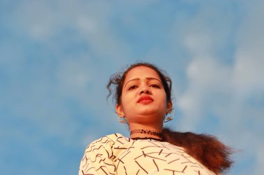 Güzel bir Hintli kadının arkasında küçük beyaz bir bulutla mavi, parlak bir gökyüzü.