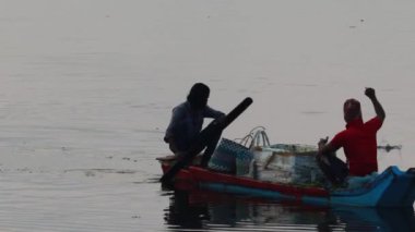 Chennai, Tamil Nadu, Hindistan. 08 Ekim 2020. Tahta bir teknede oturan iki balıkçı suya balık atıp pelikan kuşunu yiyecek olarak besliyor.