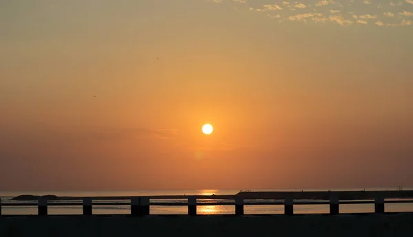 바다에서 실루엣 다리를 가로질러 하늘에 비치는 황금빛 광선으로 아름다운 사진을 — 스톡 사진