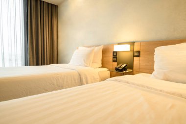 Yatak odasında beyaz çarşaflı, lambalı ve telefonlu bir çift kişilik yatak..