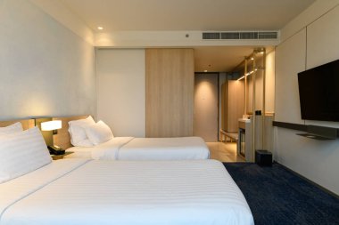 Yatak odasında beyaz çarşaflı, lambalı ve telefonlu bir çift kişilik yatak..