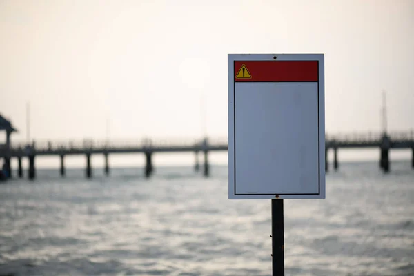 Yazısız bir uyarı işareti, kırmızı çizgili beyaz arka planda bir köprüyle denizin önüne yerleştirilir..