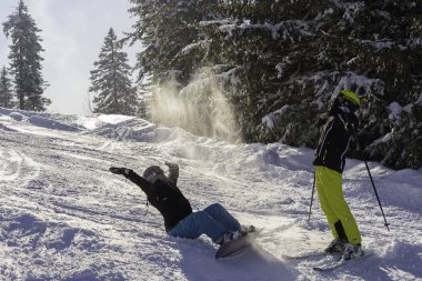 Jugendliche sitzt mit Snowboard im Schnee und wirft glcklich Pulverschnee in die Luft, Junge steht mit Ski Berghang und jauchzt vergngt in den Himmel.