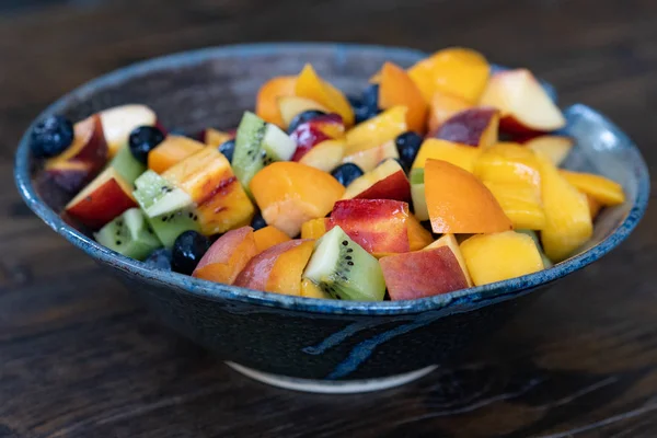 Salada de frutas frescas coloridas em tigela escura na mesa de madeira durante o dia — Fotografia de Stock