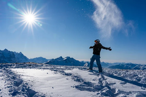 Girl enjoying sunbeams in winter while throwing snow in the air at top of the mountain range. Snowboarder in late afternoon in the Swiss alps in winter. Spectacular view, for concept.