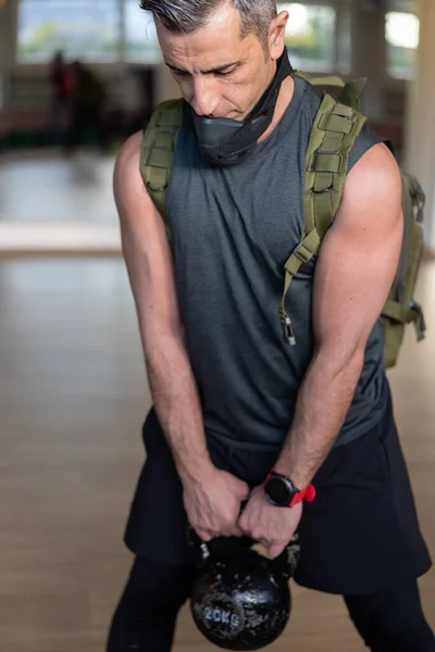 Acemi birliği eğitmeni spor salonundaki spor aletleriyle ayakta duruyor. Eğitim maskesi, dambıl, kum torbası, halat ve lastik bant taşıyın. Beden eğitimi konsepti portresi.