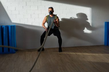 Antrenman maskesi takan bir sporcu. Kapalı bir yerde, meşe zemininde, güneş ve gölgeyle. Eğitim kampı konsepti.