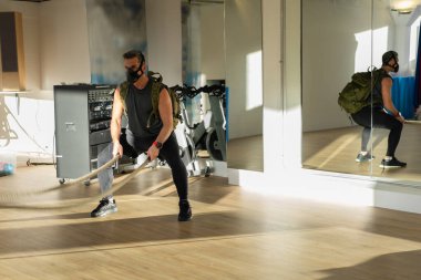 Antrenman maskeli savaş halatları sporcusu. Kapalı bir yerde, meşe zemininde, güneş ve gölgeyle. Eğitim kampı konsepti.