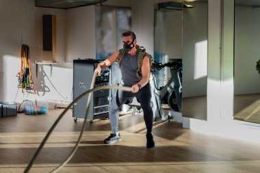 Antrenman maskeli savaş halatları sporcusu. Kapalı bir yerde, meşe zemininde, güneş ve gölgeyle. Eğitim kampı konsepti.