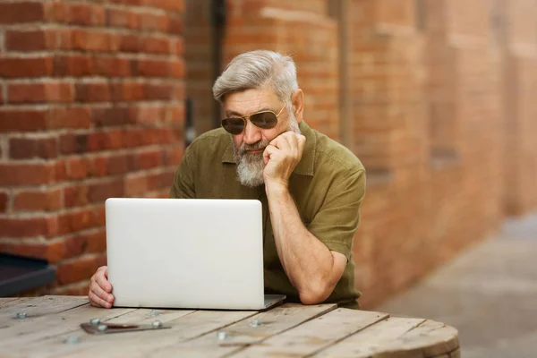 Gray adult businessman hipster in casual clothes sitting on the street near the office and unhappy and tired of working at a laptop