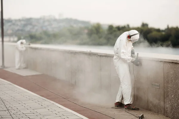 A man in a white protective suit and respirator grinds the concrete slabs of the waterfront