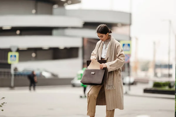 A beautiful businesswoman of Asian appearance pulls out a folder with documents from a leather briefcase