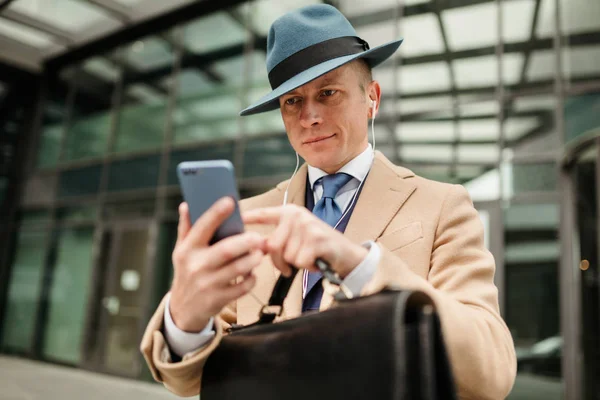 The man in the hat types a text message on his smartphone