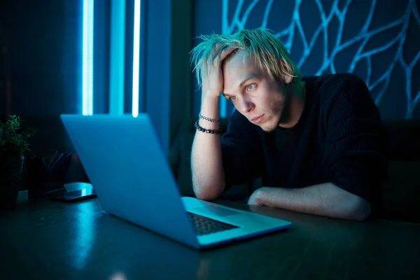 Hipster blond guy sitting at the table in front of a laptop and the disappointment was shocked to learn of her loss