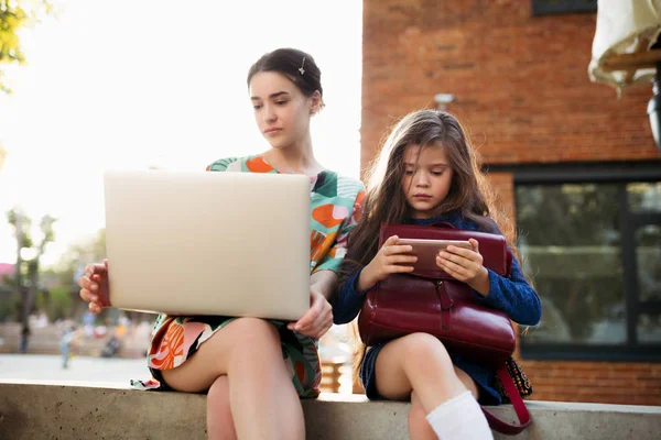 Mom with a laptop in her hands makes Internet purchases and sits next to the daughter of preschool age and watching cartoons