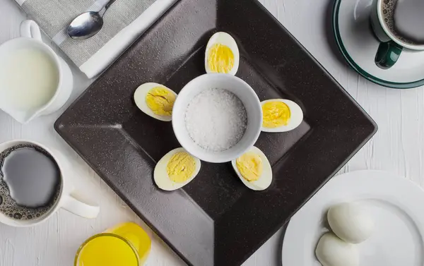 Jaja gotowane na brązowym talerzu z kawą, śmietaną i sokiem pomarańczowym oraz solą — Zdjęcie stockowe