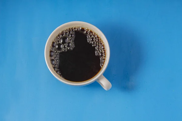 Café negro sobre una taza blanca con un fondo azul —  Fotos de Stock
