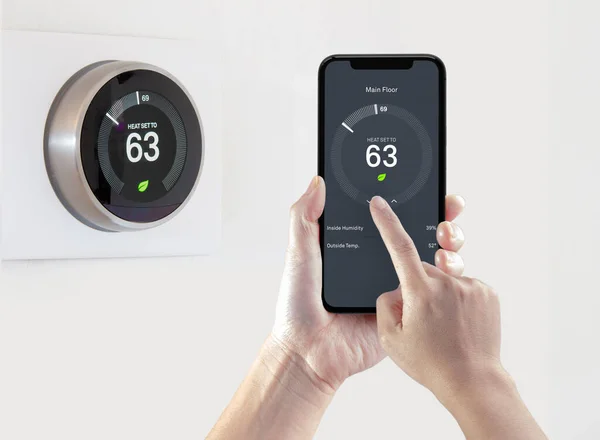 Beyaz arka planda kablosuz akıllı termostat ile enerji tasarrufu sağlayan akıllı bir telefon uygulaması kullanan bir kişi.
