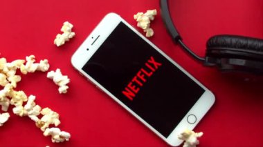 Netflix logosu ile iPhone Plus 'ın üzerine düşen patlamış mısırın yavaş hareketi 120 fps' lik kırmızı bir arkaplan.